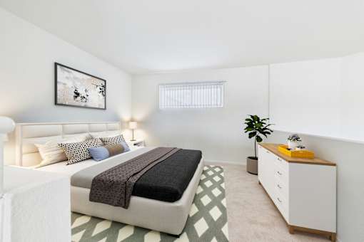 A bedroom with a bed, nightstand, and a plant.