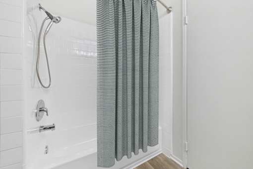 A white tiled bathroom with a shower and a grey curtain.
