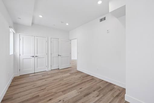 A room with white walls and wooden flooring with four white doors.