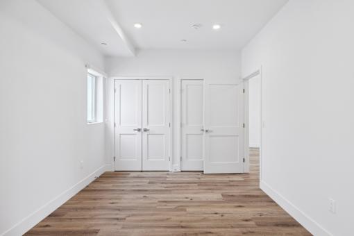 A room with white walls and wooden flooring with three white doors.