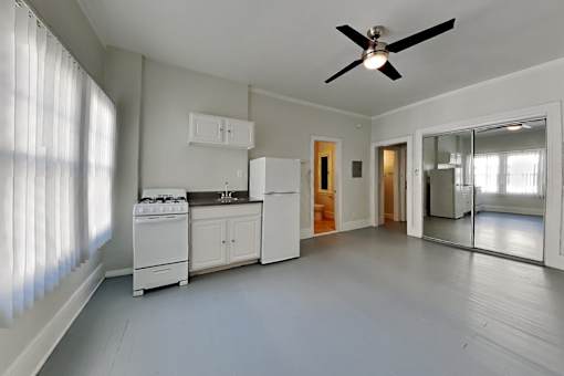 A white kitchen with a ceiling fan and a window with blinds.