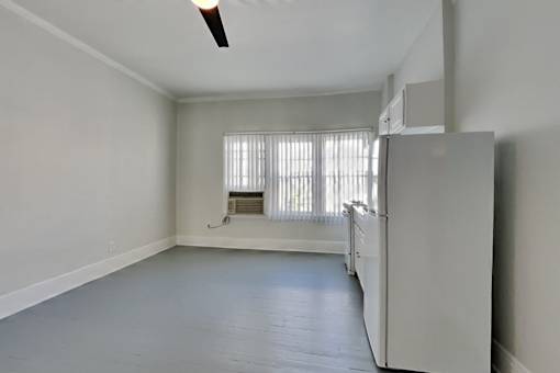 A white refrigerator sits in a room with a window and a fan.