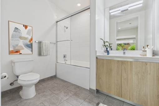 A white toilet is in a bathroom with a white tub and a wooden cabinet.