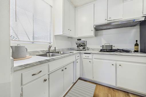 A white kitchen with a sink, stove, and cabinets.