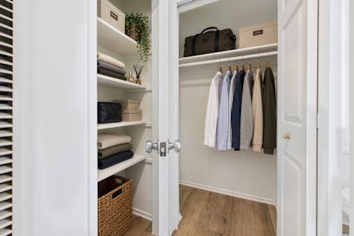 A white closet with clothes hanging and towels folded on shelves.