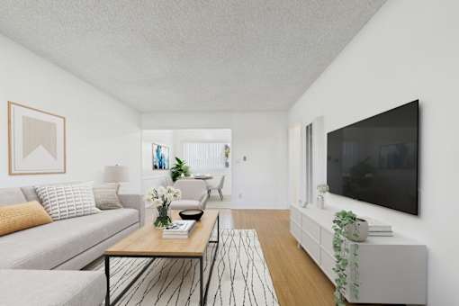 A living room with a grey couch, a coffee table, and a flat screen TV mounted on the wall.