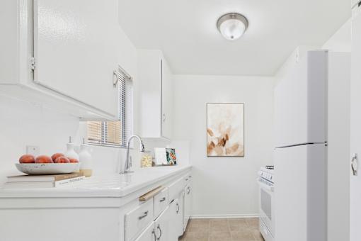 A white kitchen with a bowl of fruit on the counter.