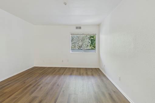 A room with wooden flooring and a window with a view of trees.