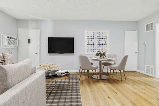 A living room with a grey couch, a coffee table, a dining table with chairs, and a television mounted on the wall.