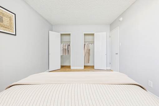A bedroom with a large bed and a wardrobe with clothes hanging in it.