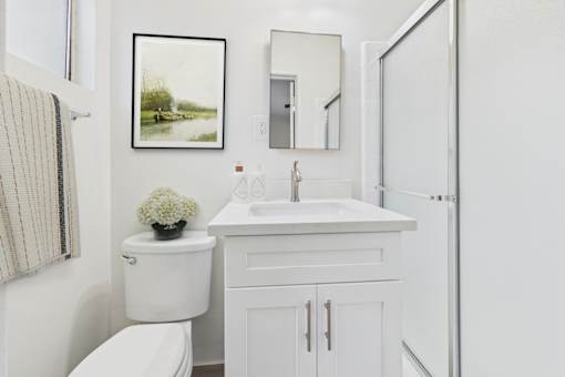 A white bathroom with a toilet, sink, and a framed picture on the wall.