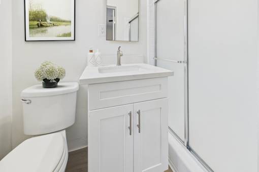 A white bathroom with a toilet, sink, and a framed picture on the wall.