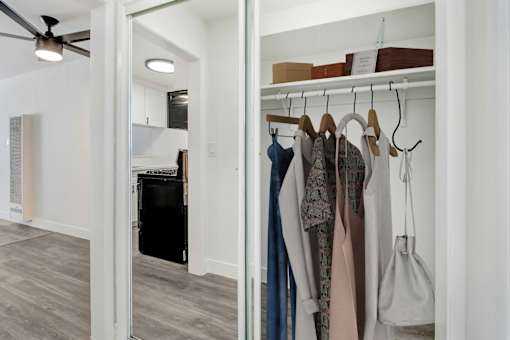 a walk in closet with a mirrored wall with clothes hanging on it