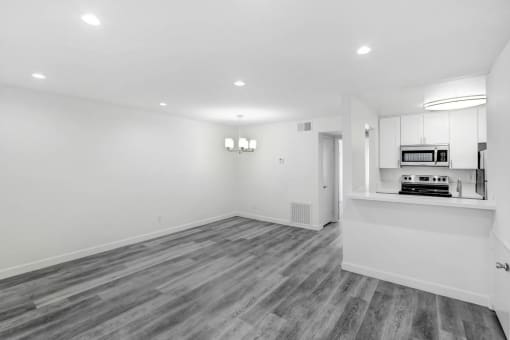 an empty living room and kitchen with white walls and wood flooring