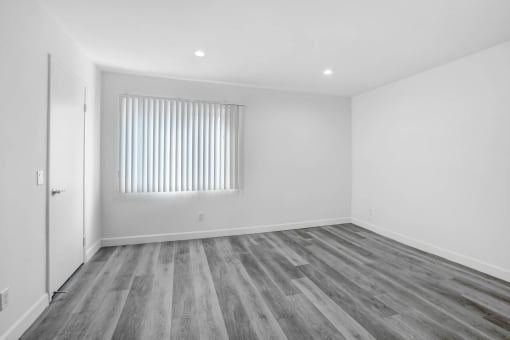 a bedroom with white walls and wood flooring and a window