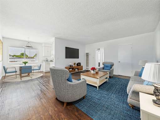A living room with a grey sofa, a grey armchair, a wooden coffee table, and a flat screen TV mounted on the wall.