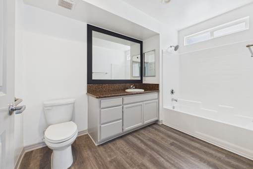 A white toilet sits in a bathroom with a wooden floor and white walls.