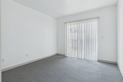 A room with a carpeted floor and a window with blinds.