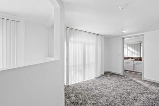A white room with a grey carpet and a doorway leading to another room.