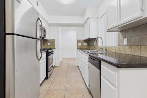 A kitchen with white cabinets and a black fridge.
