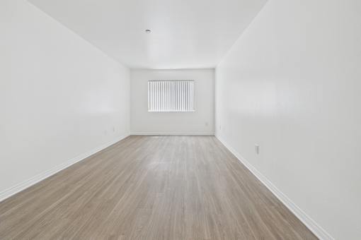 A room with wooden flooring and a white wall with a vent.
