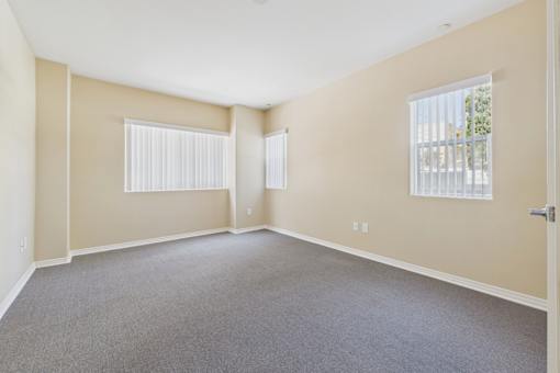 A room with a carpeted floor and two windows.