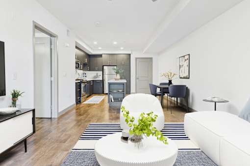 A modern living room with a white couch, a coffee table, and a dining area in the background.