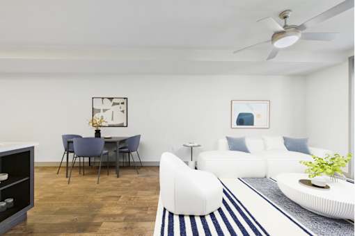 A living room with a white couch, a dining table with chairs, and a ceiling fan.