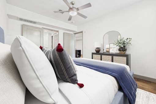 A white bed with a red pillow and a blue blanket.
