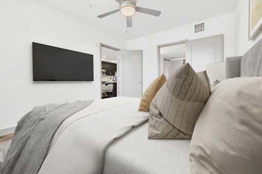 A bedroom with a bed, pillows, and a television on the wall.