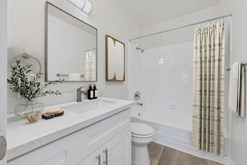 A white bathroom with a toilet, sink, mirror, and shower.