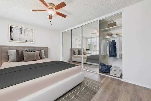 A bedroom with a bed, a ceiling fan, and a closet with a mirror.