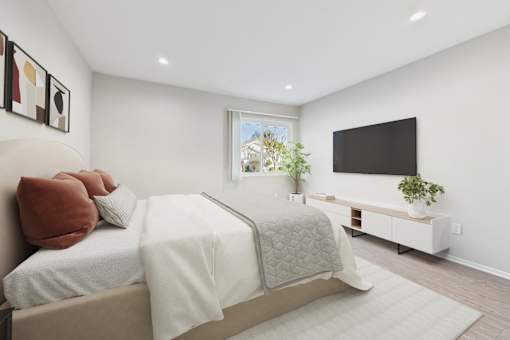 A bedroom with a bed, pillows, a blanket, a window, a plant, and a TV.