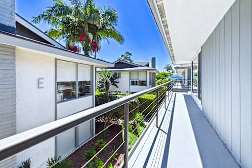 A white building with a balcony and a tree in the background.