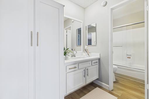 A white bathroom with a sink, mirror, and cabinets.