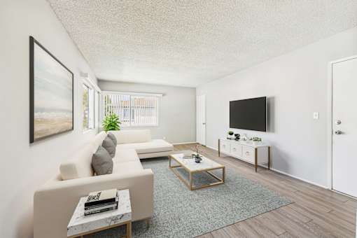 A living room with a white couch, a coffee table, and a flat screen TV mounted on the wall.