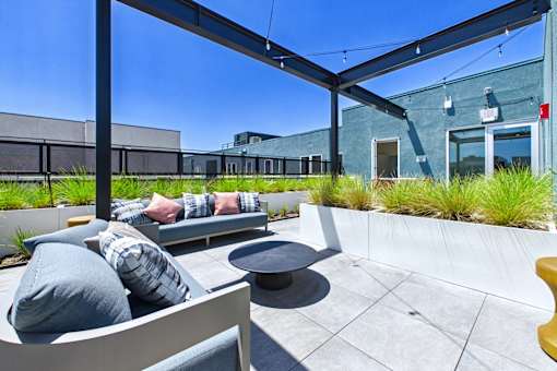 A patio with a couch and pillows under a black awning.