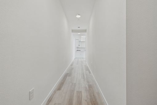 A long hallway with white walls and wood flooring.