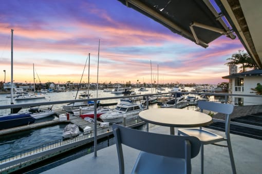a view of a marina at sunset from a balcony with a table and chairs