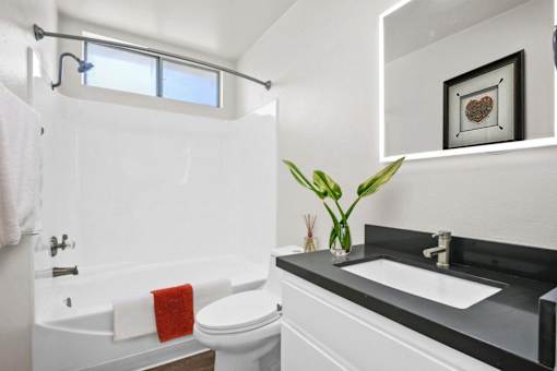 A white bathroom with a black counter top and a red towel.