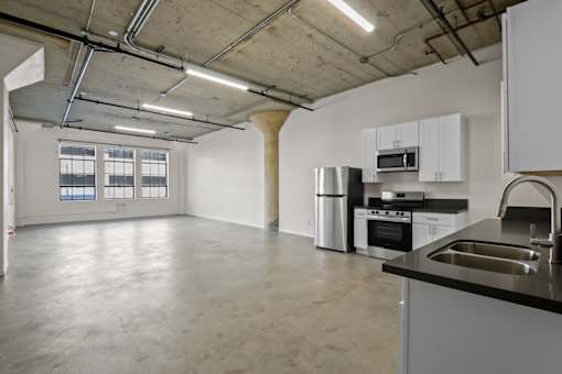 A kitchen with a sink, stove, and oven in a large empty room.
