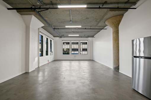A large empty room with a curved concrete ceiling and a stainless steel refrigerator on the right side.