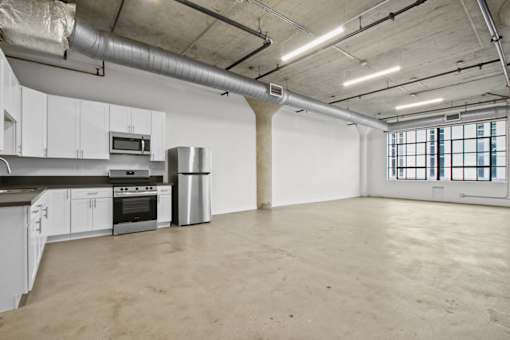 A large empty room with a kitchen area to the left.