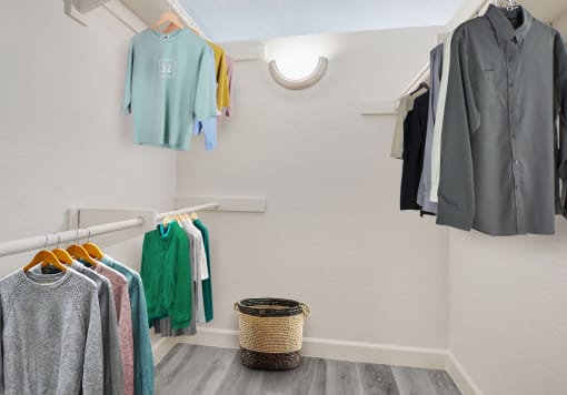 a walk in closet with clothes hanging on the wall