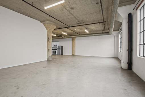 A large, empty room with concrete floors and walls, and a few pieces of furniture.