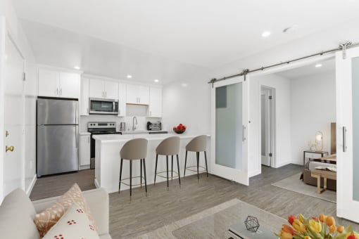 a living area with a kitchen and a bar with three chairs