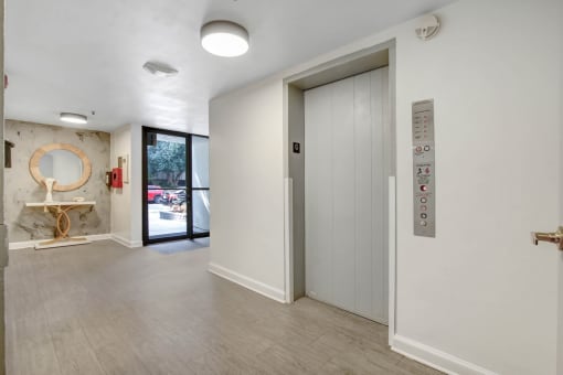 a room with a door that leads to a hallway with a mirror and a sink