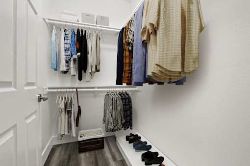 A white closet with clothes hanging and shoes on the floor.