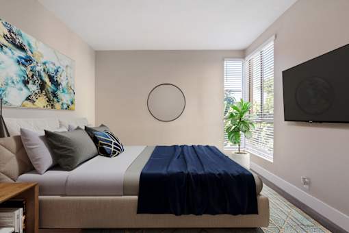 A bedroom with a bed, a painting, a plant, and a television.