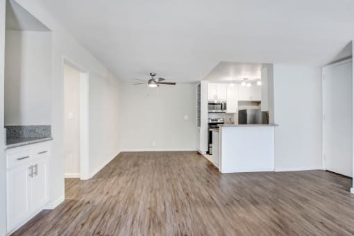 the living room of an apartment with a kitchen and a ceiling fan